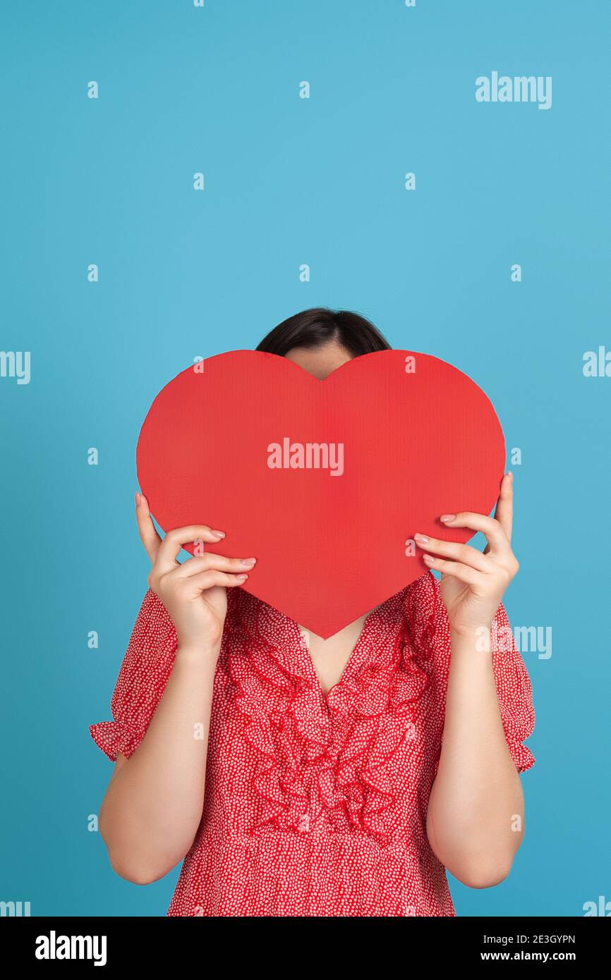 a dark-haired woman in a red dress hides her face behind a large red ...