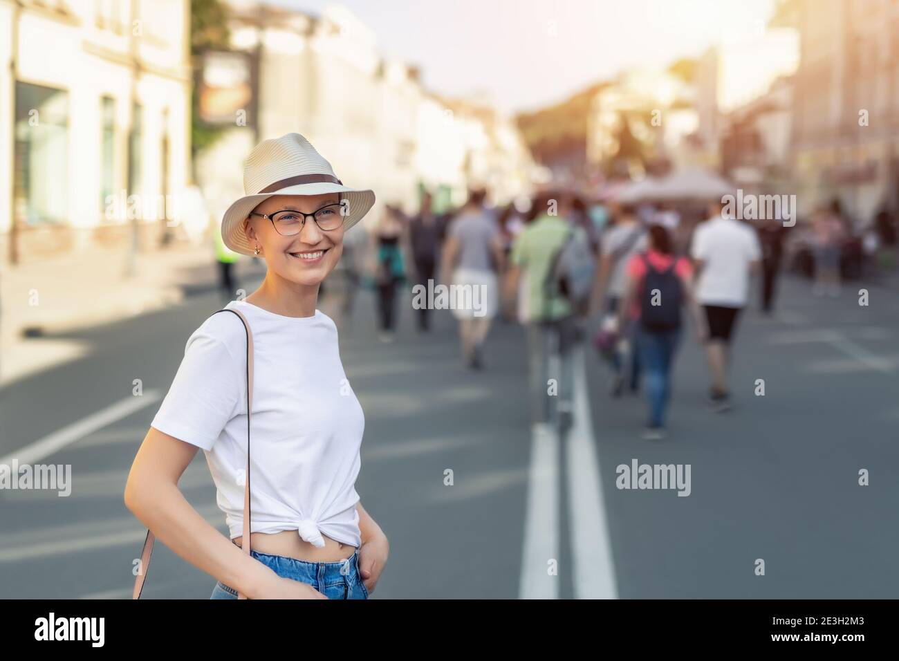Young adult beautiful stylish single skinhead woman in white t-short, hat and jeans enjoy walking shopping city street on warm summer sunny day. Happy Stock Photo