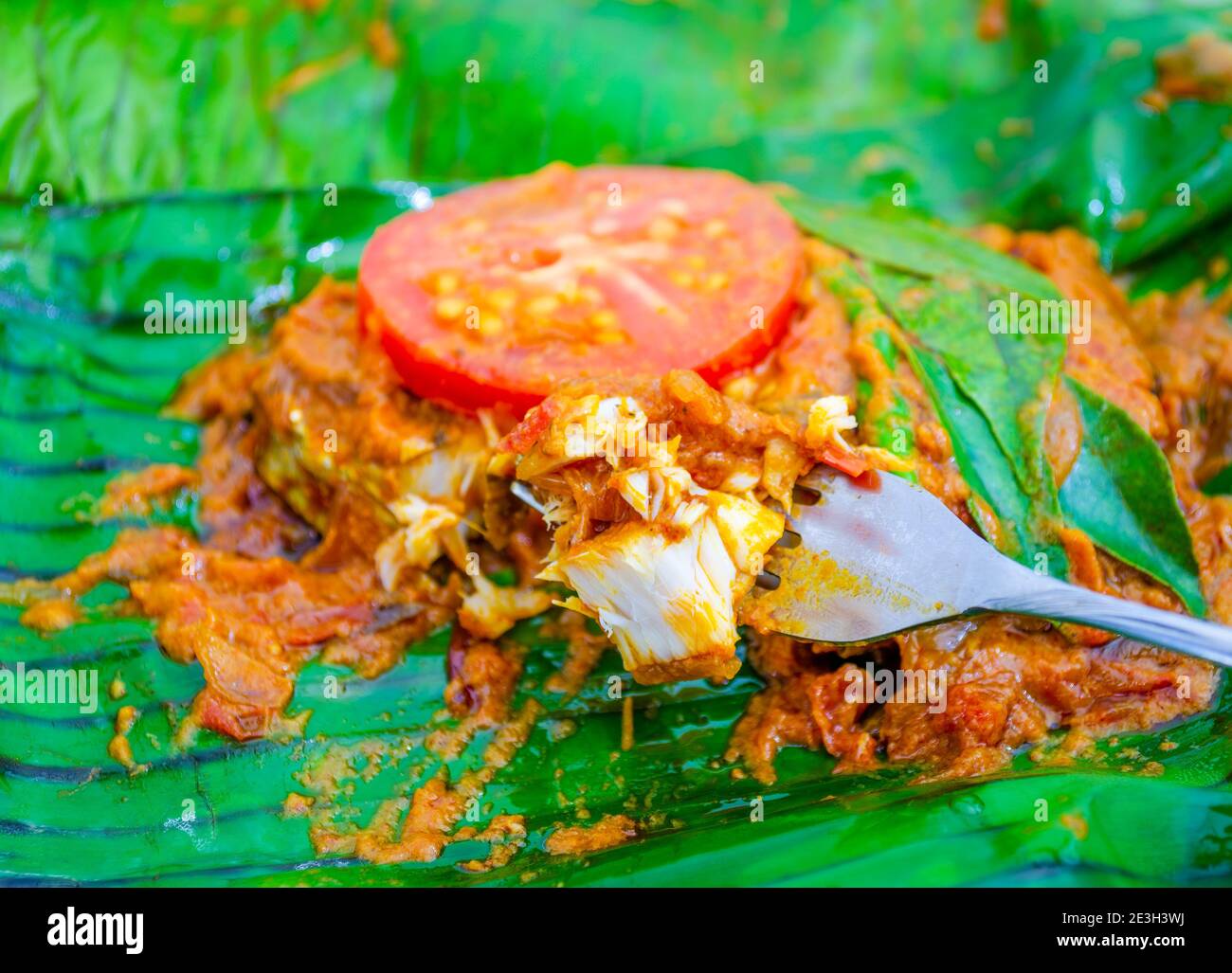 Closeup of banana leaf fried fish taken on a fork to be eaten. A true Kerala style preparation, this spicy meen pollichathu. Stock Photo