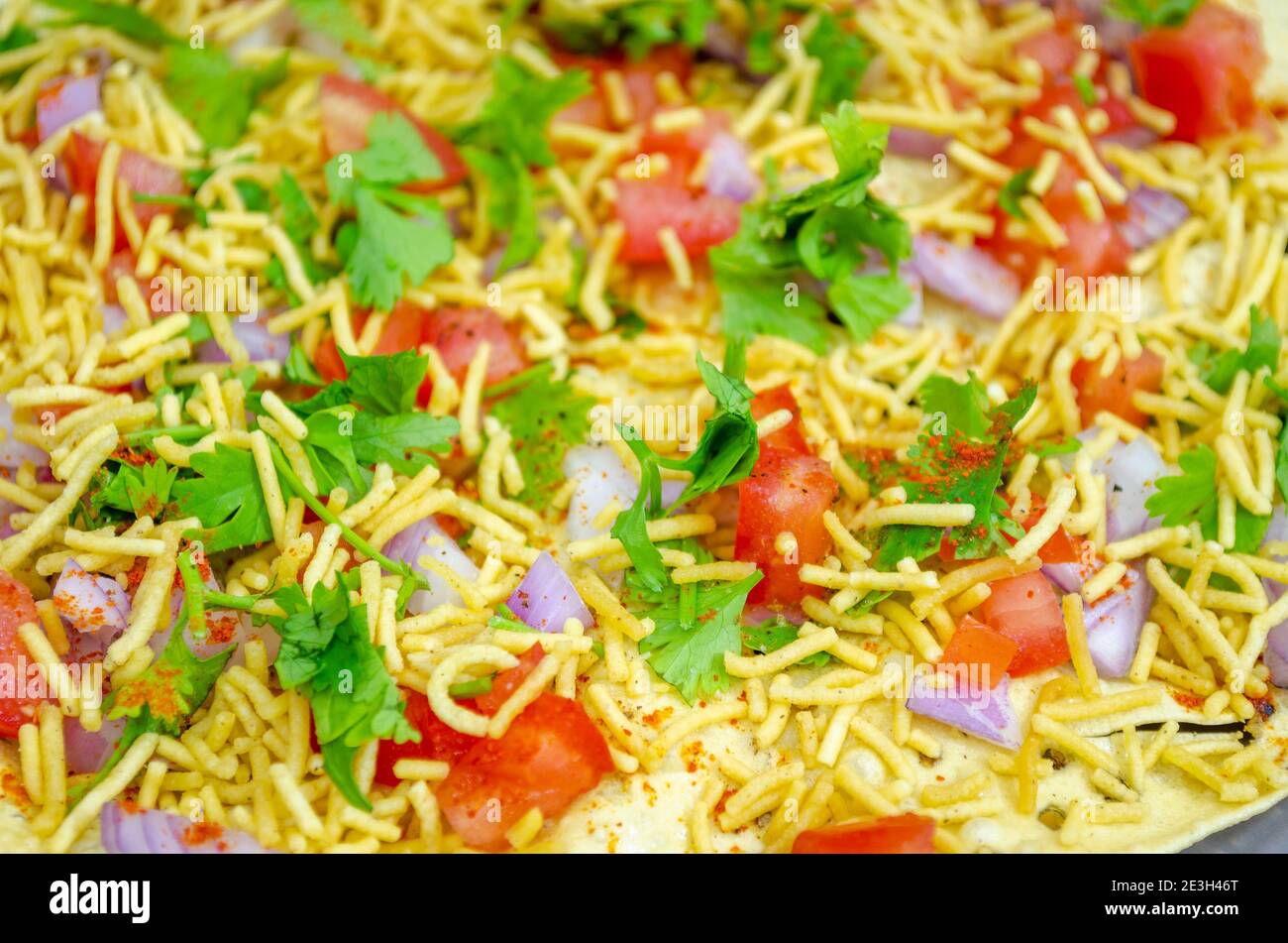 Closeup of masala papad spread with onions, tomatoes, sev, coriander leaves, etc. A background ideal for restaurants & coffee shops Stock Photo