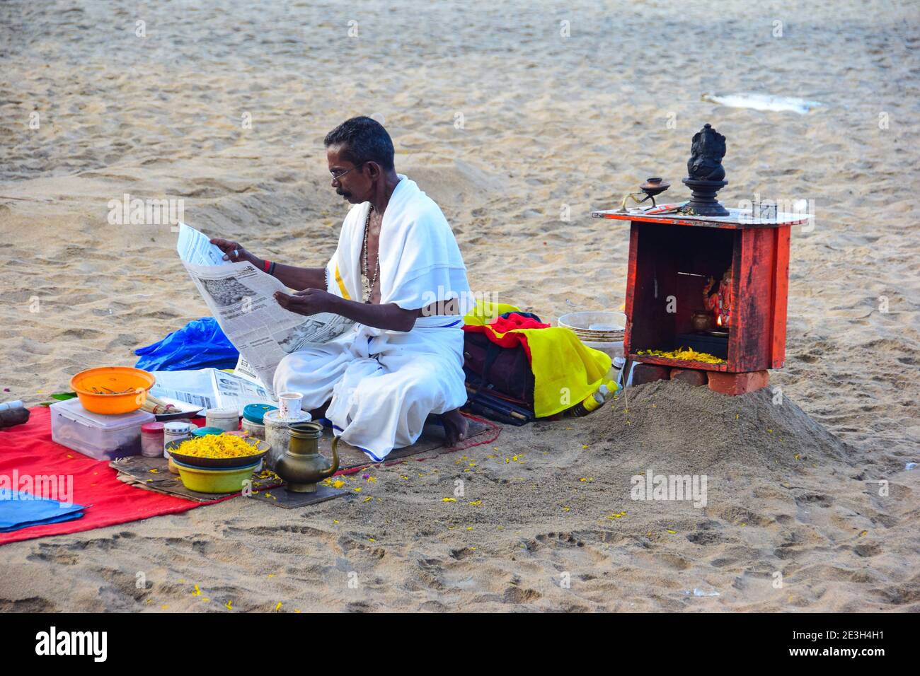 Hindu Priest reading newspaper, before washing away sins of pilgrims, Varkala Beach, Varkala, Kerala, India Stock Photo