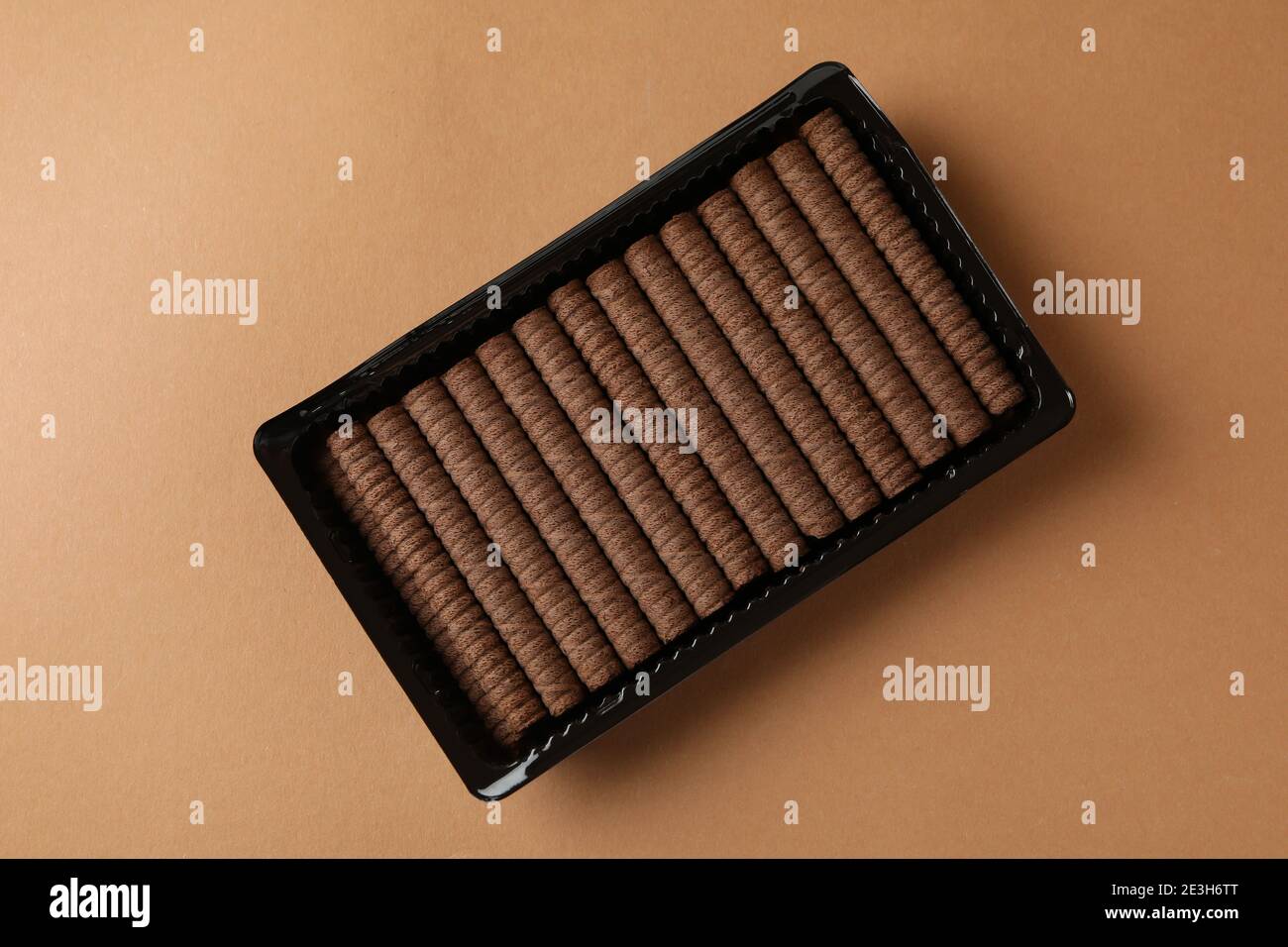 Plastic box with chocolate wafer rolls on brown background Stock Photo