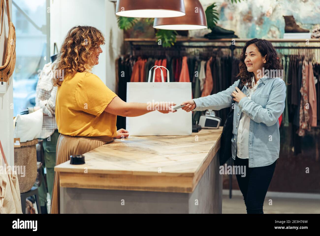 Woman giving her credit card for a contactless payment in the fashion store. Female customer paying for the purchase with credit card at clothing stor Stock Photo