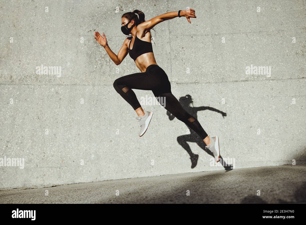Fitness woman wearing face mask running outdoors. Woman athlete exercising outdoors in morning. Stock Photo