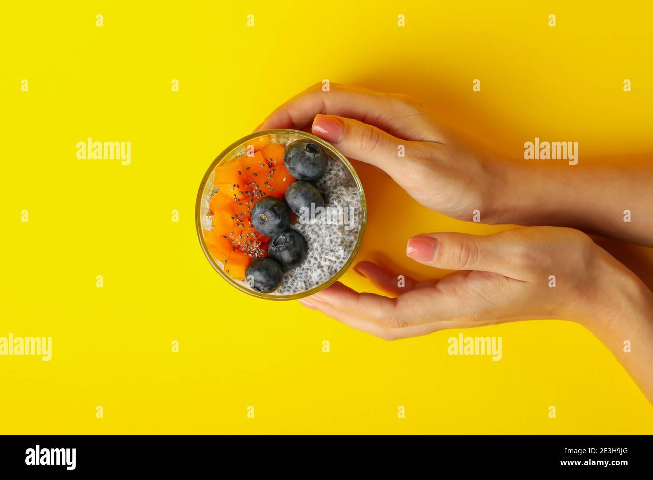 Female hands hold glass of chia pudding on yellow background Stock
