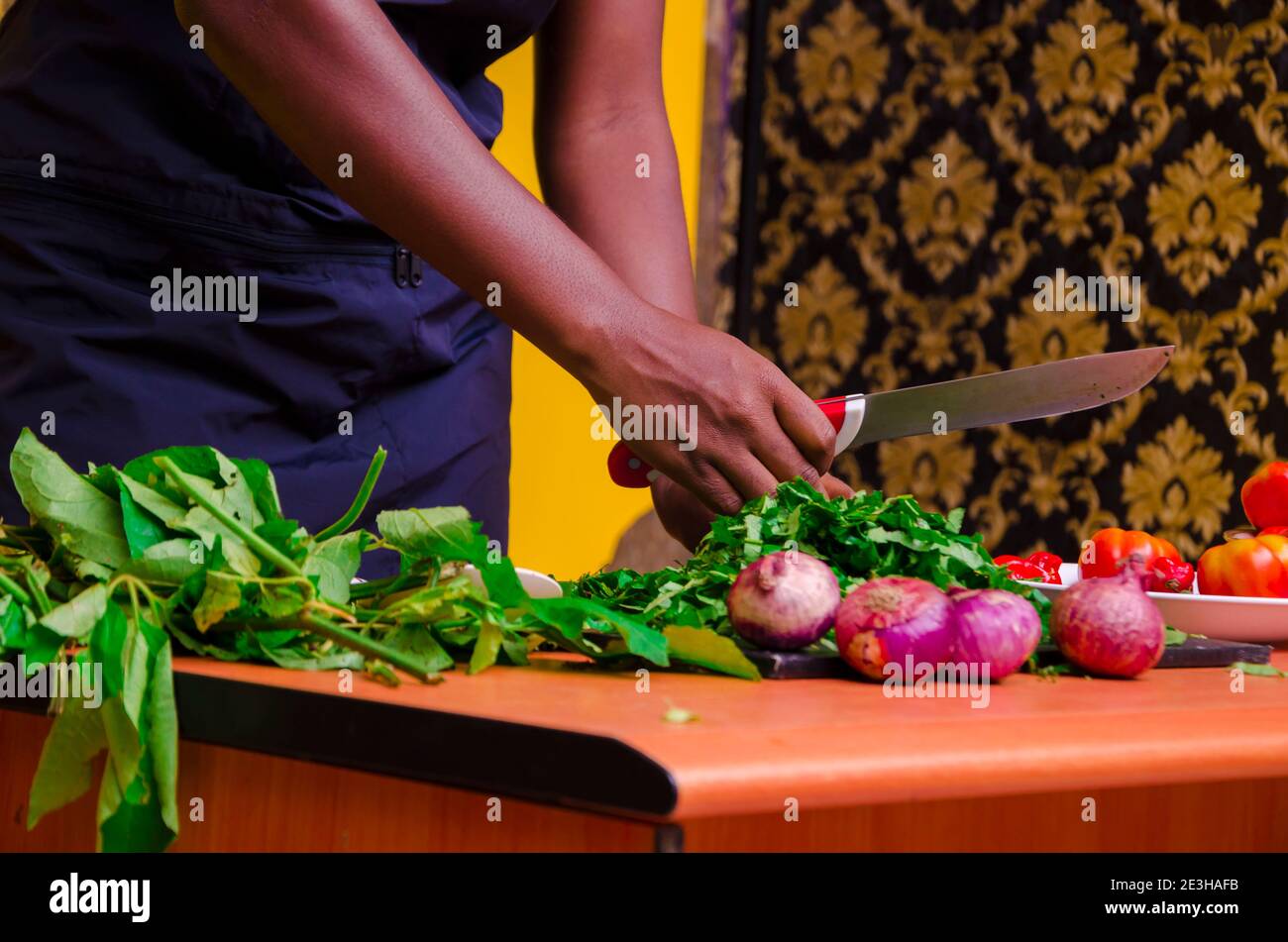 African chef carefully cutting vegetables with knife on the table Stock Photo