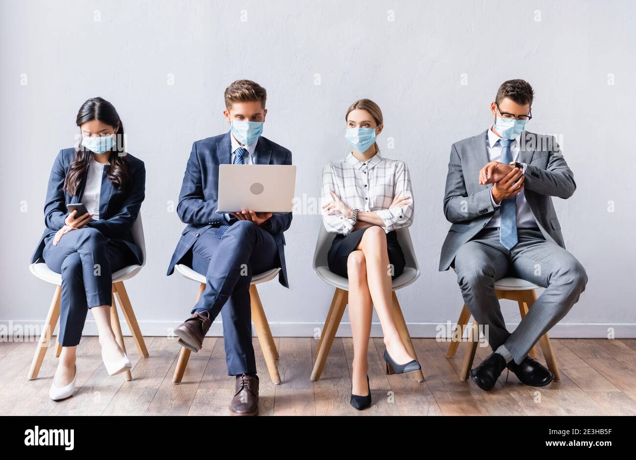 Multiethnic businesspeople in medical masks using devices before job interview Stock Photo