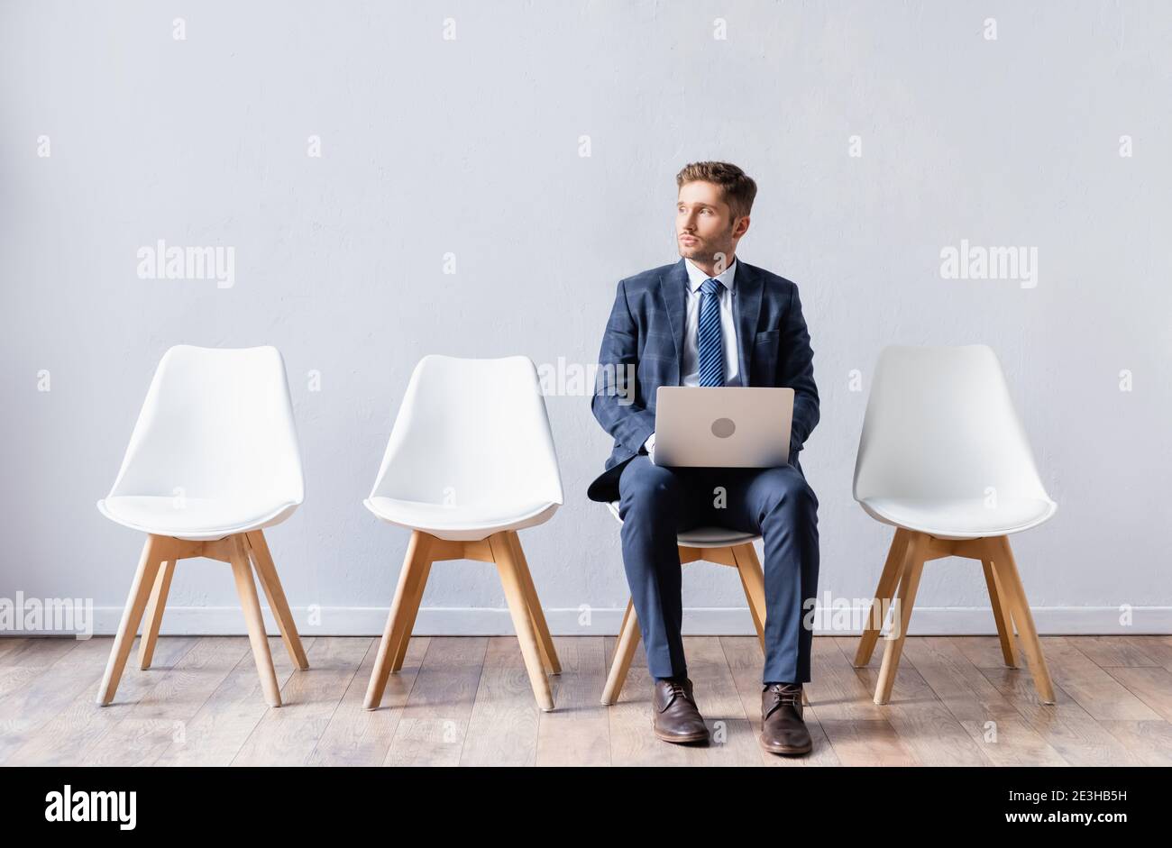 Businessman with laptop sitting on chair in hall Stock Photo