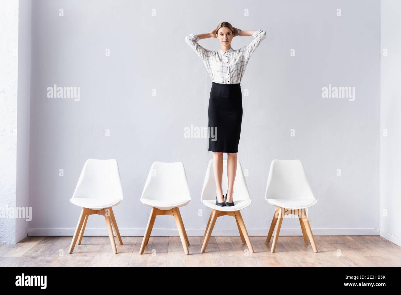 Businesswoman standing on chair and looking at camera in office hall Stock Photo