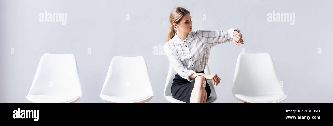 Businesswoman looking at wristwatch on chair in office, banner Stock Photo