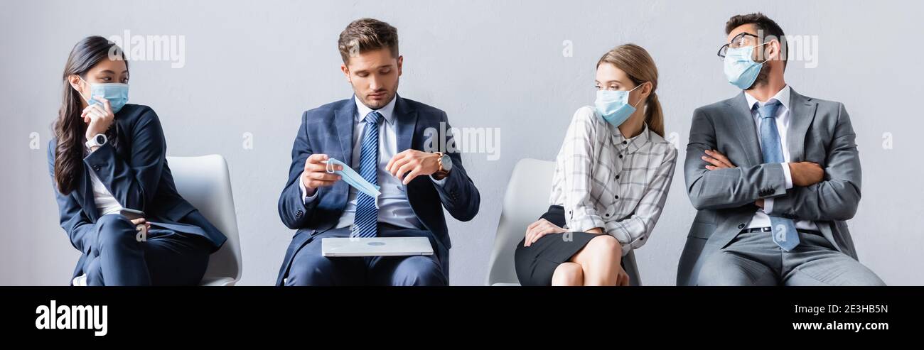 Multiethnic businesspeople looking at colleague with laptop holding medical mask in hall, banner Stock Photo