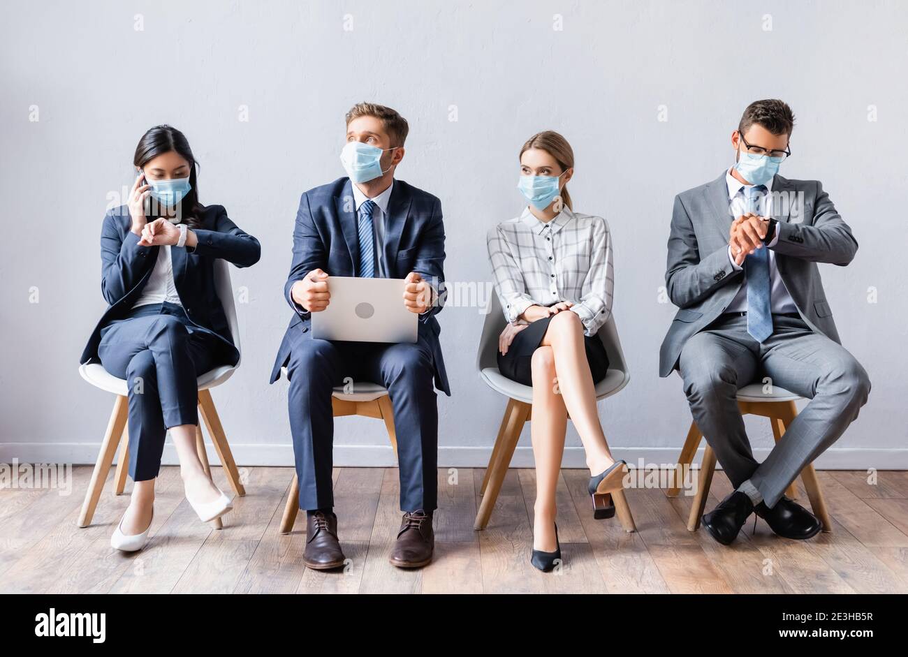 Multicultural people in medical masks with laptop and smartphone waiting on chairs in hall Stock Photo