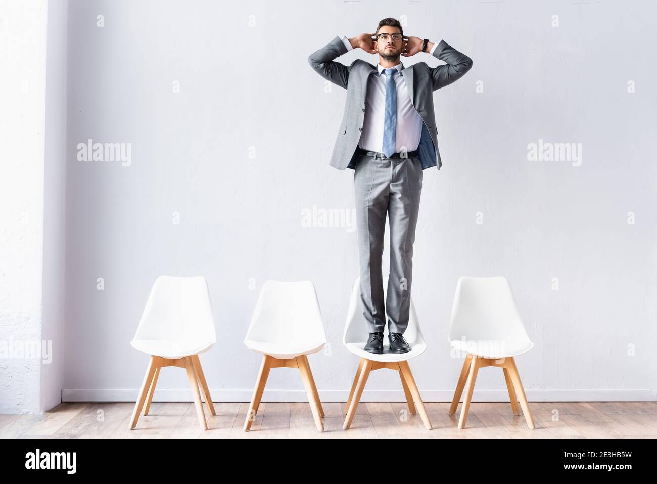 Businessman standing on chair near wall in office Stock Photo