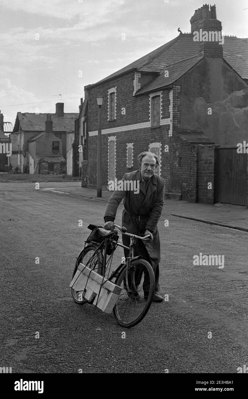 A man pushing his bike through streets of bricked up houses awaiting demolition, Splott, Cardiff, Wales, 1974 Stock Photo