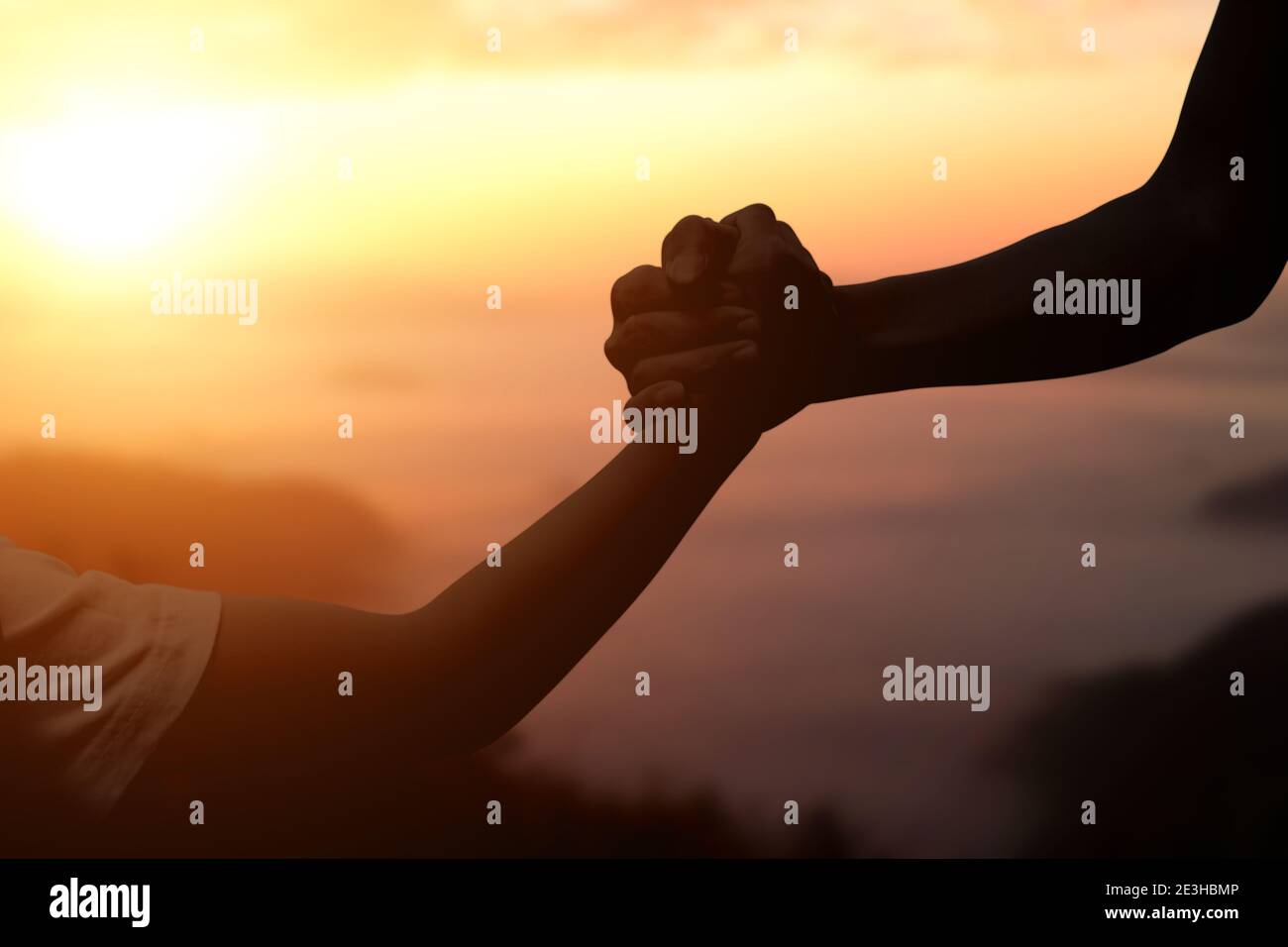 Silhouette of giving a helping hand, hope and support each other over sunset background. Stock Photo