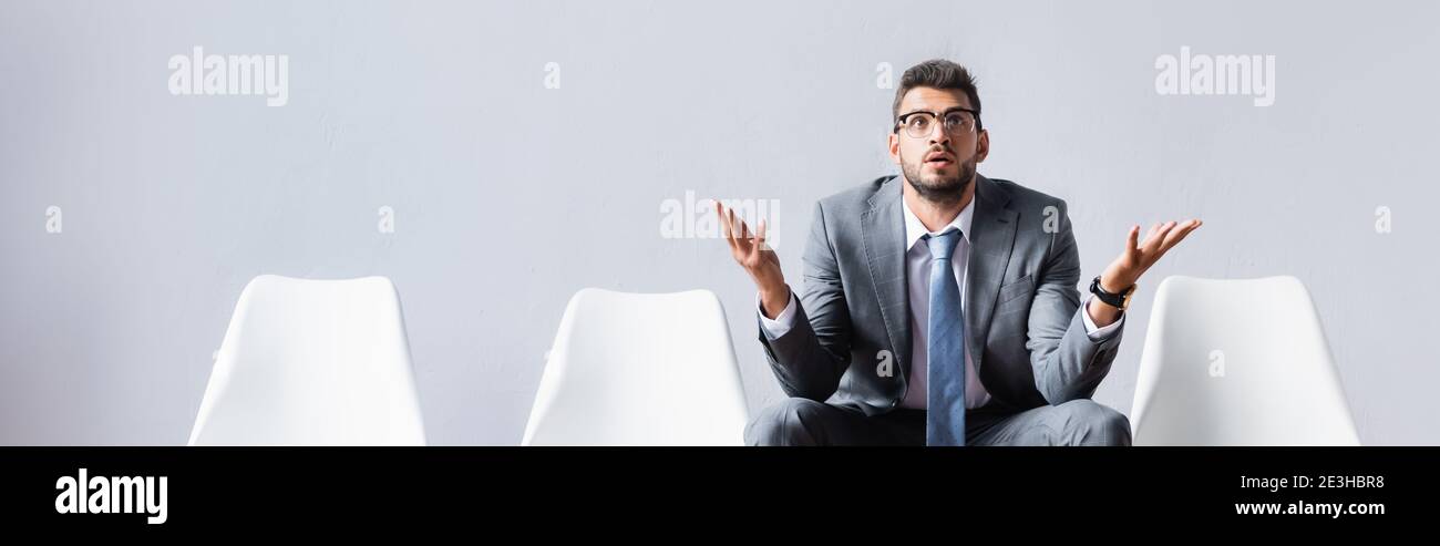 Businessman pointing with hands while waiting on chair in office, banner Stock Photo