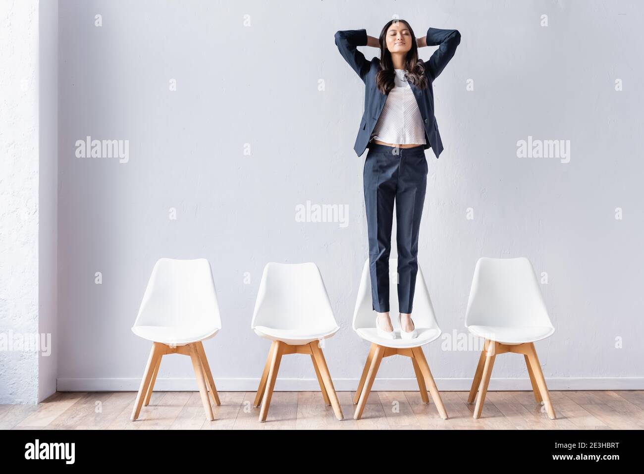 Asian businesswoman standing with closed eyes on chair in office Stock Photo