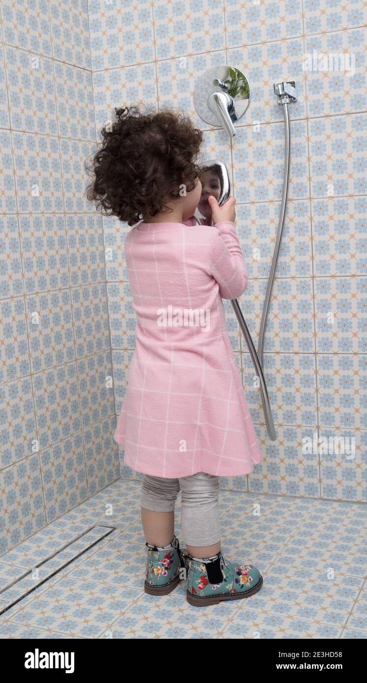 Fully dressed, toddler girl plays in the shower Stock Photo