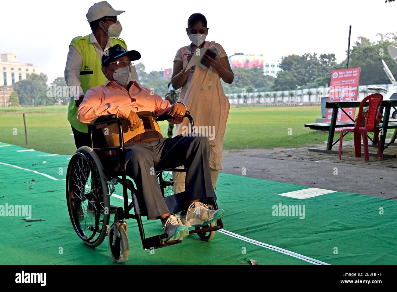 A polling worker takes an aged voter to the polling booth on a wheelchair. Stock Photo