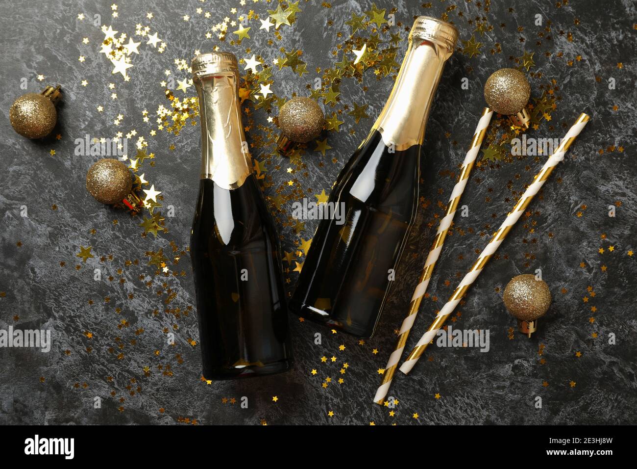 Champagne bottles, glitter and straws on black smokey background Stock