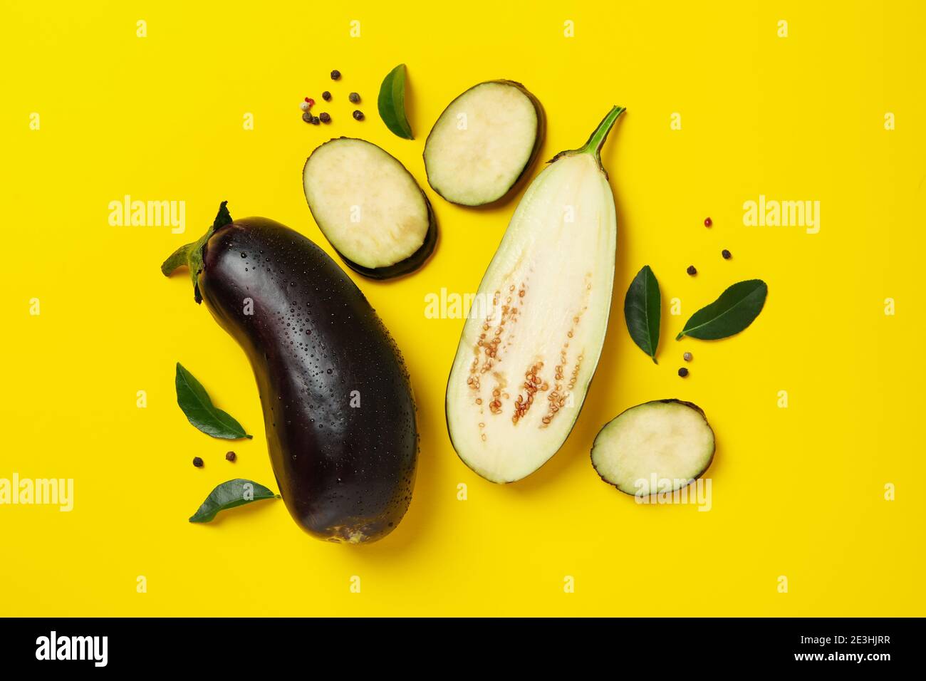 Fresh raw eggplants with water drops on yellow background Stock Photo