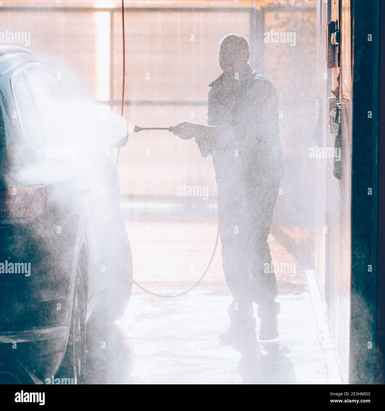Man washes car at car wash, pours water from hose. Sunlight and water