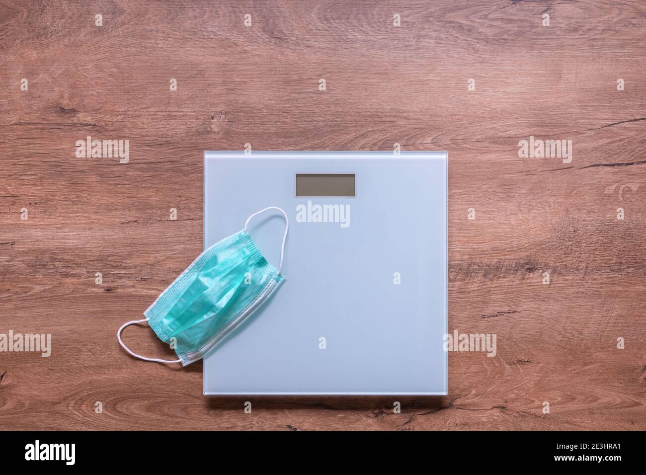 Electronic weight scale with medical protective mask on wooden floor. Weight gain during quarantine. Diet, fitness, and weight loss concept Stock Photo