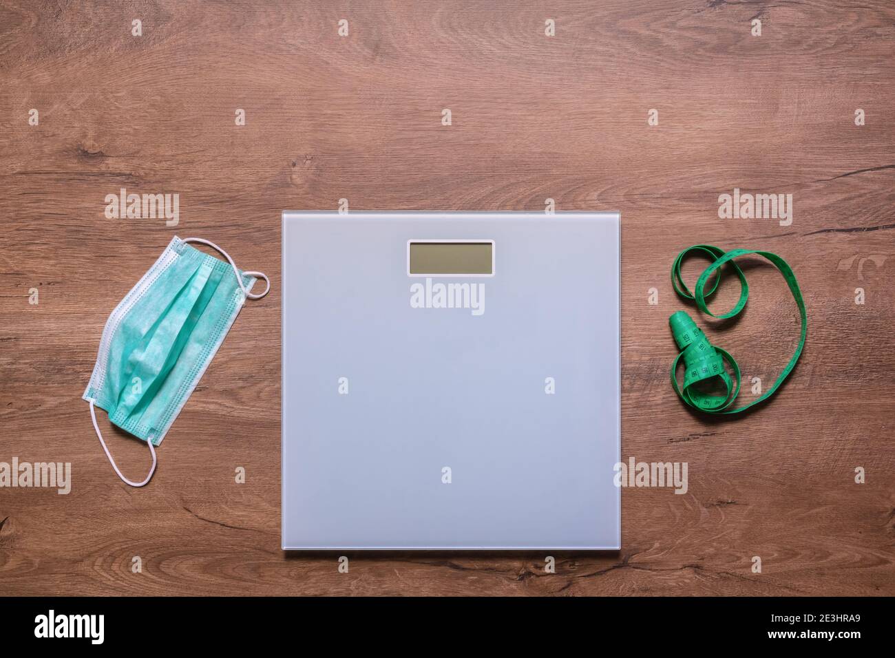 Weight scale, protective mask, and measuring tape on wooden floor. Weight gain during quarantine. Diet, fitness, and weight loss concept Stock Photo