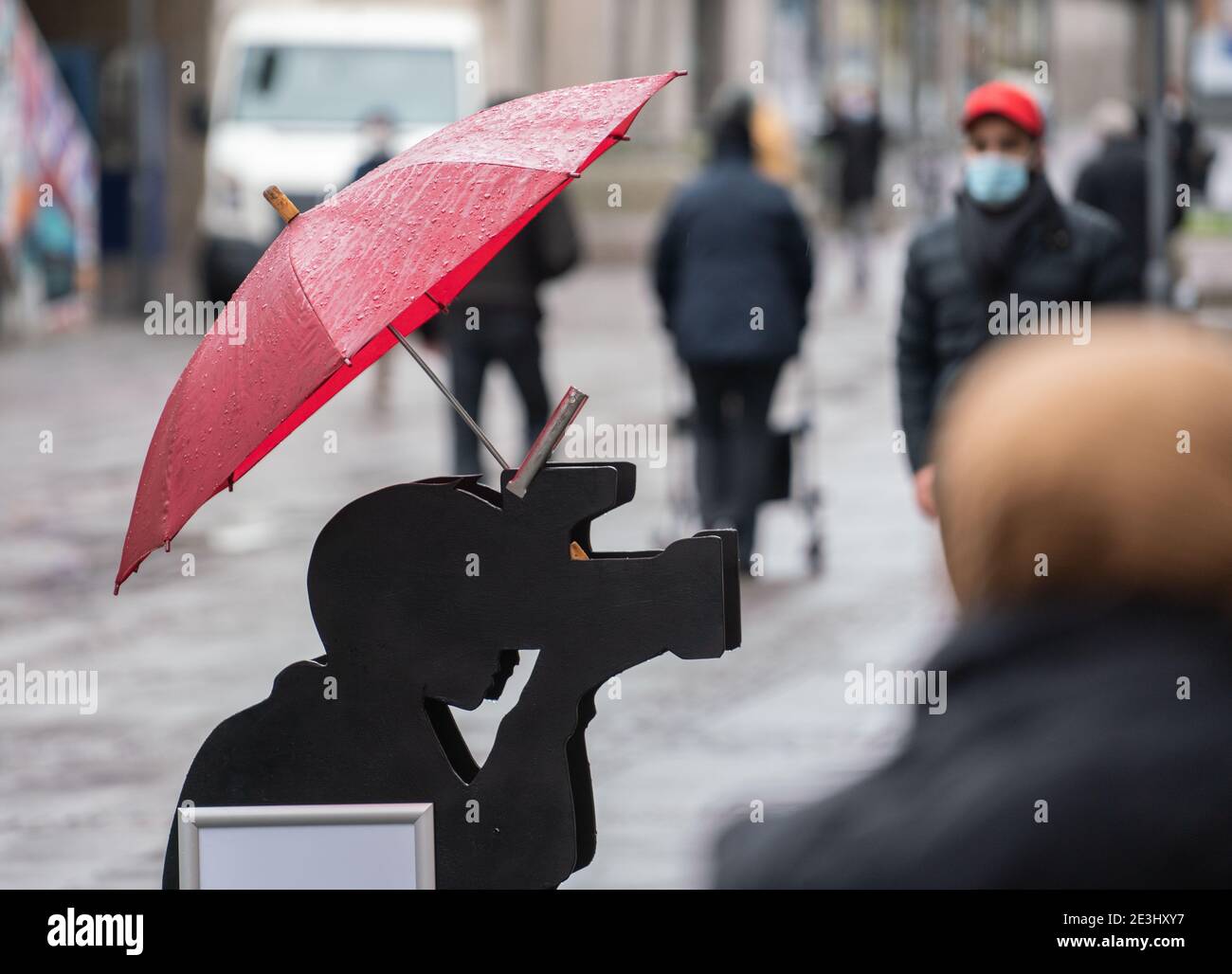 Darmstadt, Germany. 19th Jan, 2021. With the black figure of a photographer  under an umbrella, a passport photo studio in the Innnestadt advertises for  customers in rainy weather. Credit: Frank Rumpenhorst/dpa/Alamy Live