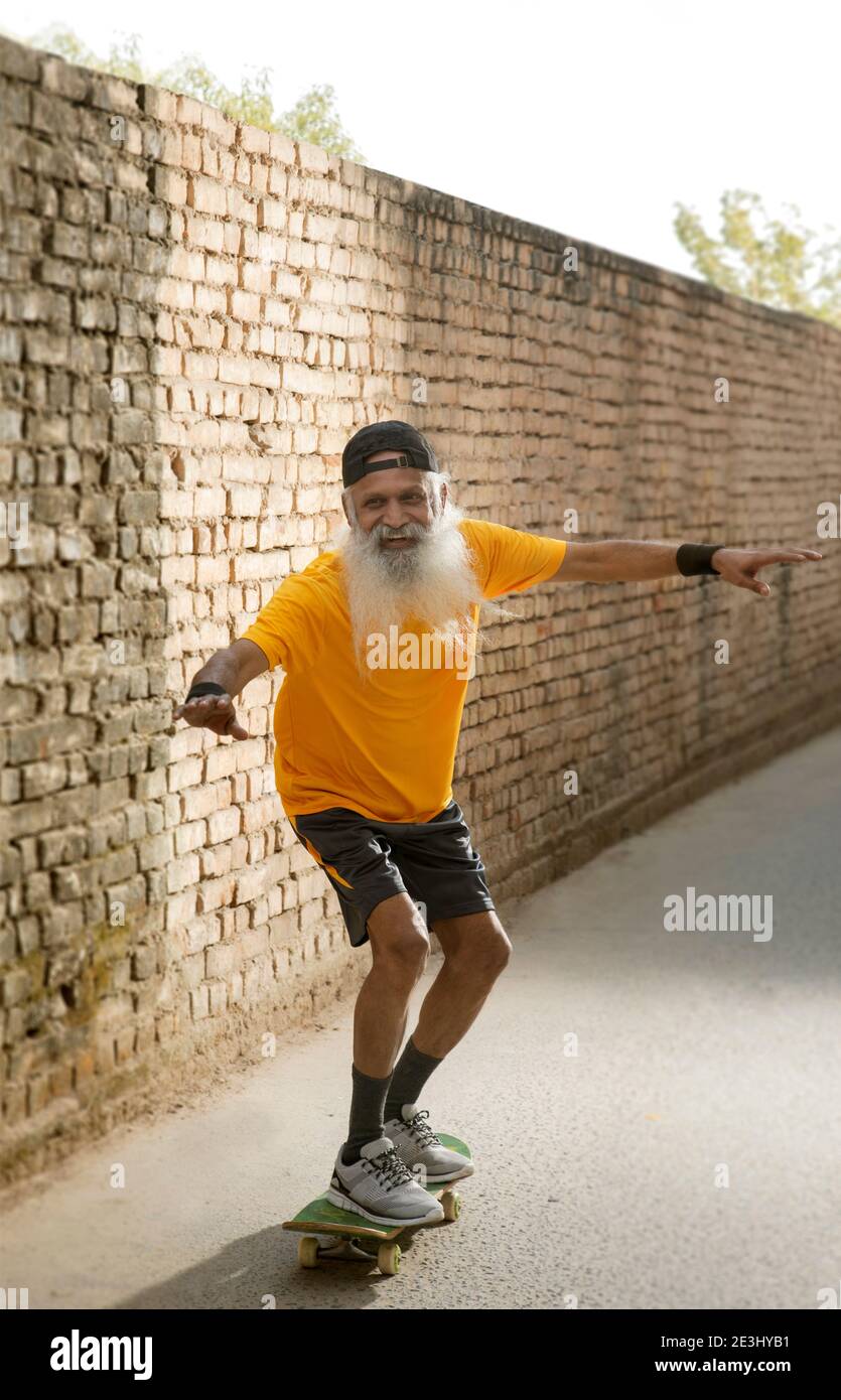 A BEARDED OLD MAN HAPPILY STANDING ON A SKATE BOARD Stock Photo