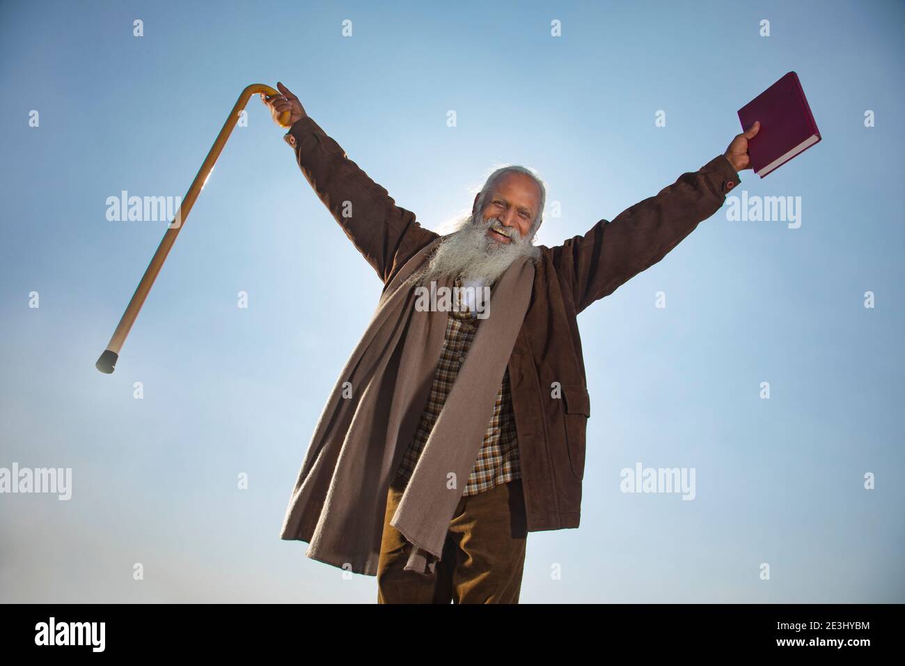 A BEARDED OLD MAN LOOKING AT CAMERA WHILE HAPPILY RAISING HANDS Stock Photo