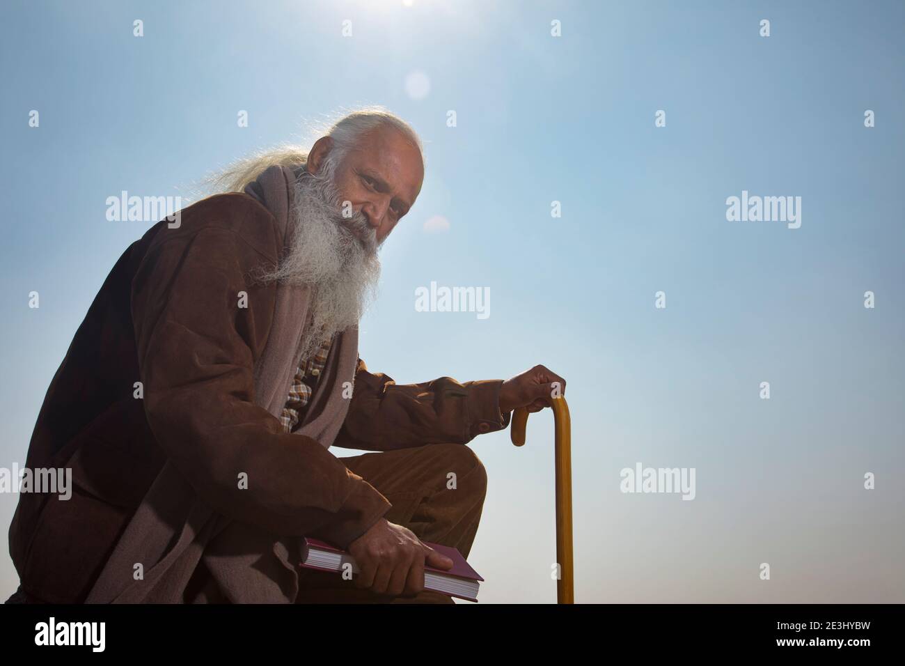 A BEARDED OLD MAN SITTING WITH SUPPORT OF STICK HOLDING A BOOK Stock Photo