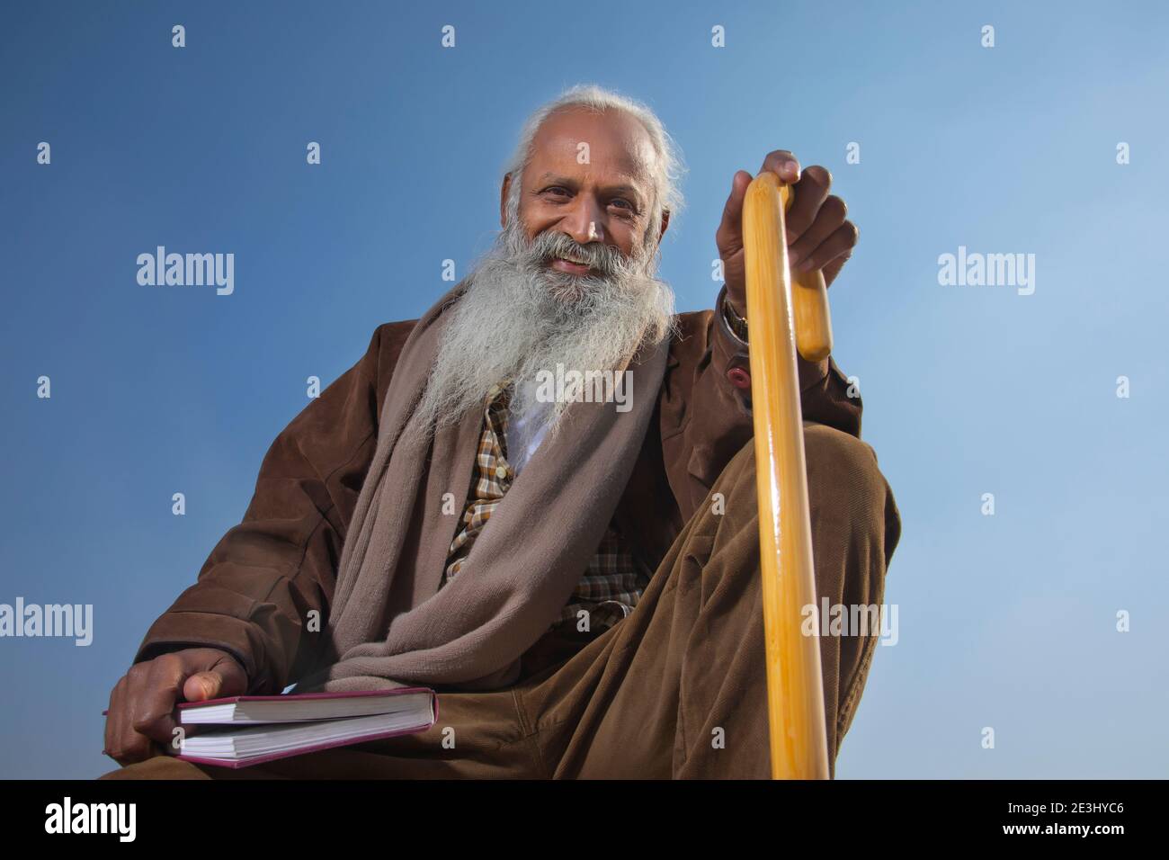 AN OLD MAN SITTING WITH BOOK HOLDING STICK SMILING AND LOOKING AT CAMERA Stock Photo