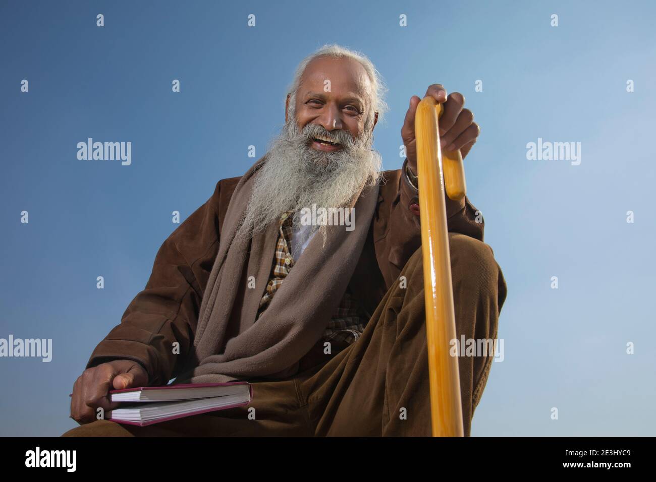 A BEARDED OLD MAN HAPPILY SITTING WITH BOOK IN ONE HAND Stock Photo