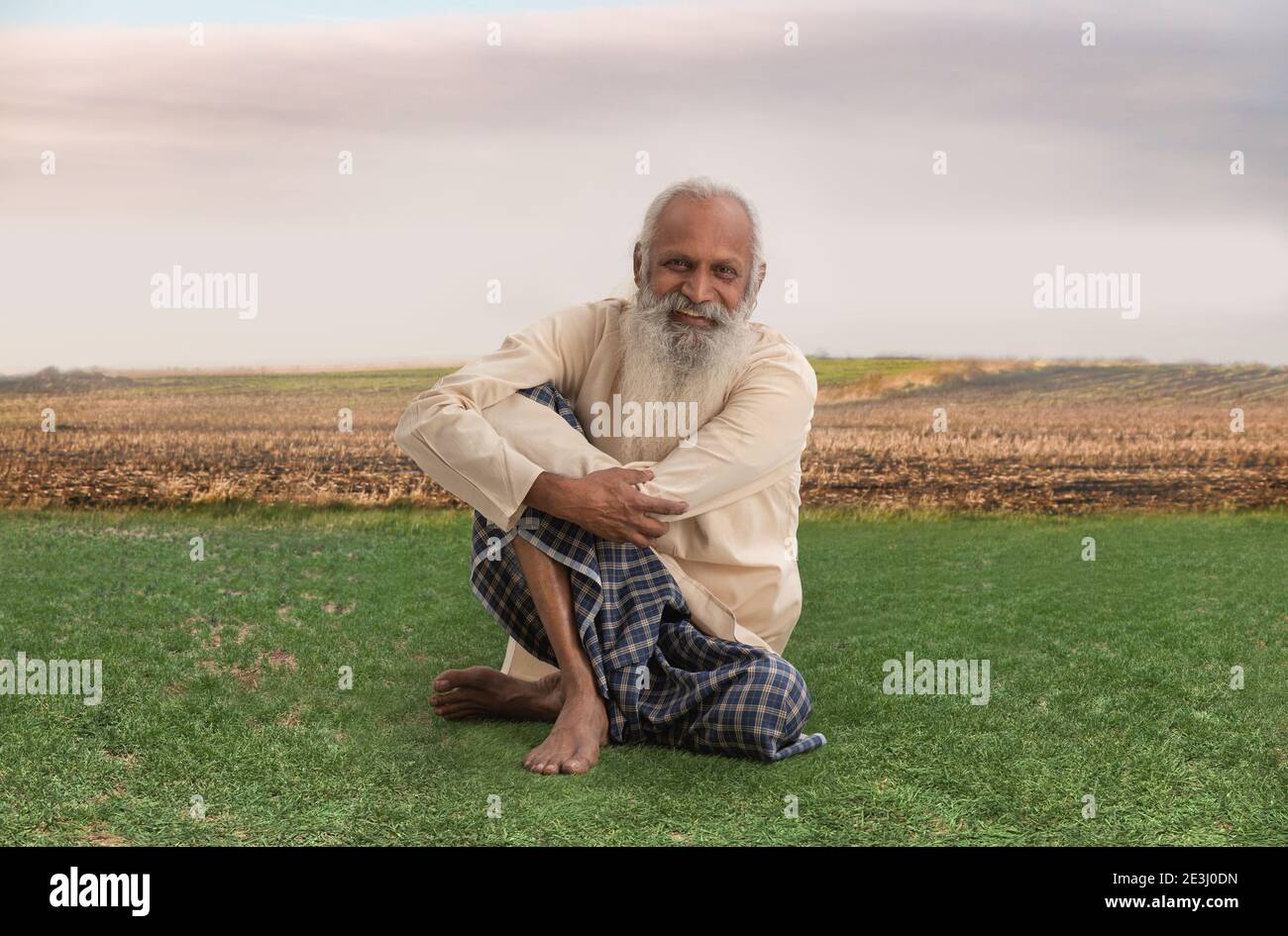AN OLD FARMER HAPPILY SITTING ON GRASSLAND Stock Photo