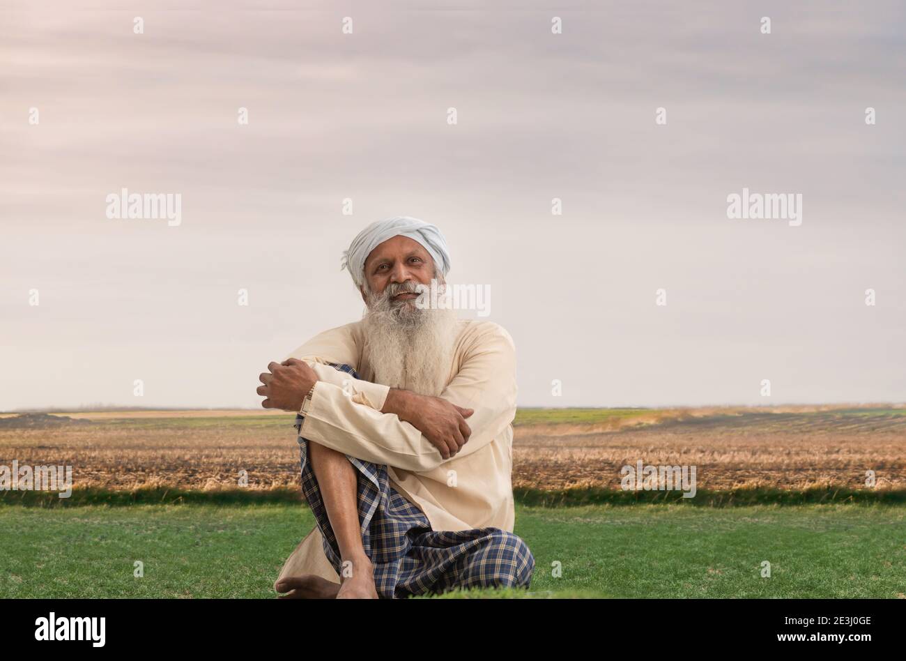 A HAPPY OLD FARMER SITTING ON FARMLAND AND LOOKING ABOVE Stock Photo