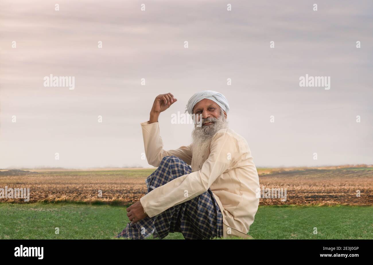 A HAPPY FARMER SITTING ON A FIELD AND LOOKING ABOVE Stock Photo