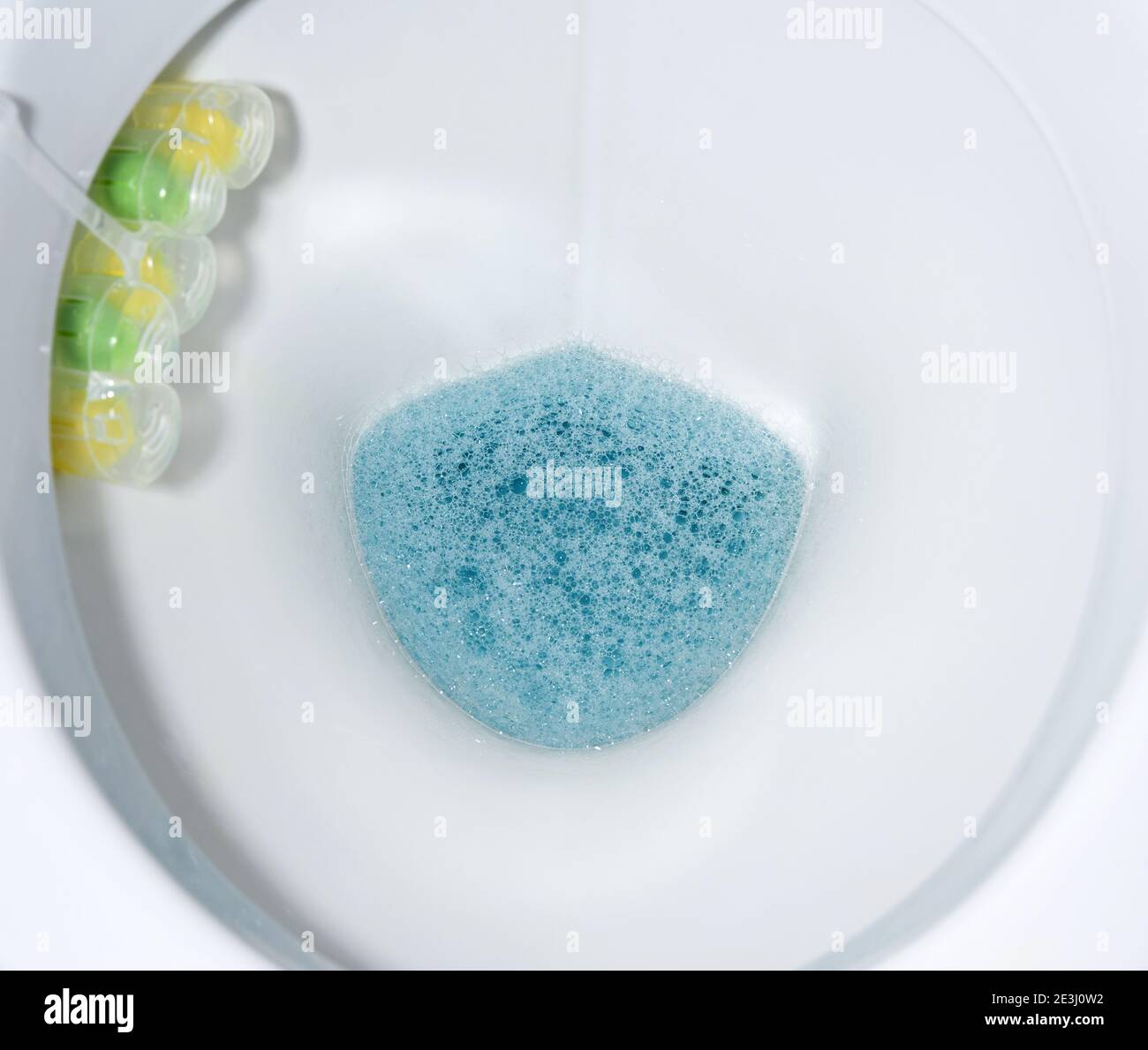 bottom of white toilet bowl with blue water and solid disinfectants