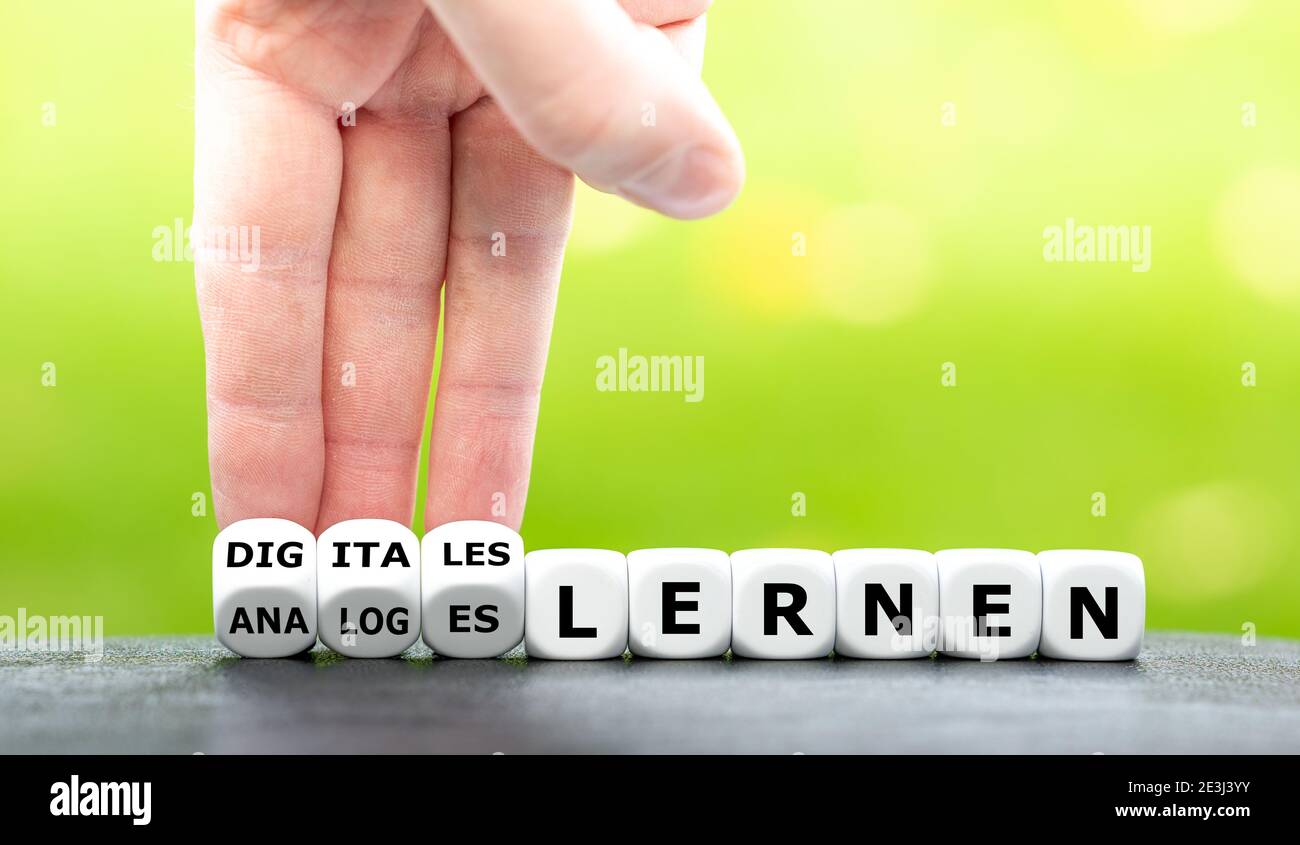 Hand turns dice and changes the German expression 'analoges lernen' (analog learning) to 'digitales lernen' (digital learning). Stock Photo