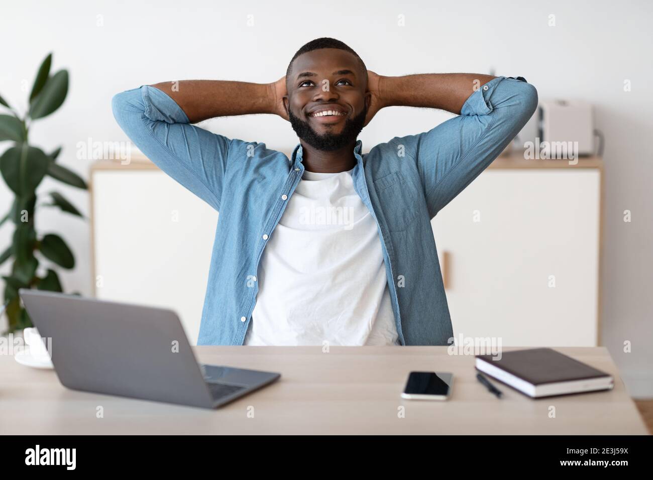 Positive Black Male Freelancer Leaning Back In Chair, Resting At