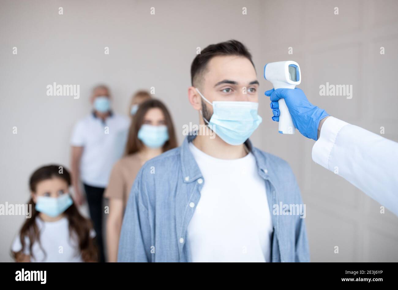Medical worker checking young man's temperature with infrared thermometer at hospital. Coronavirus vaccination Stock Photo