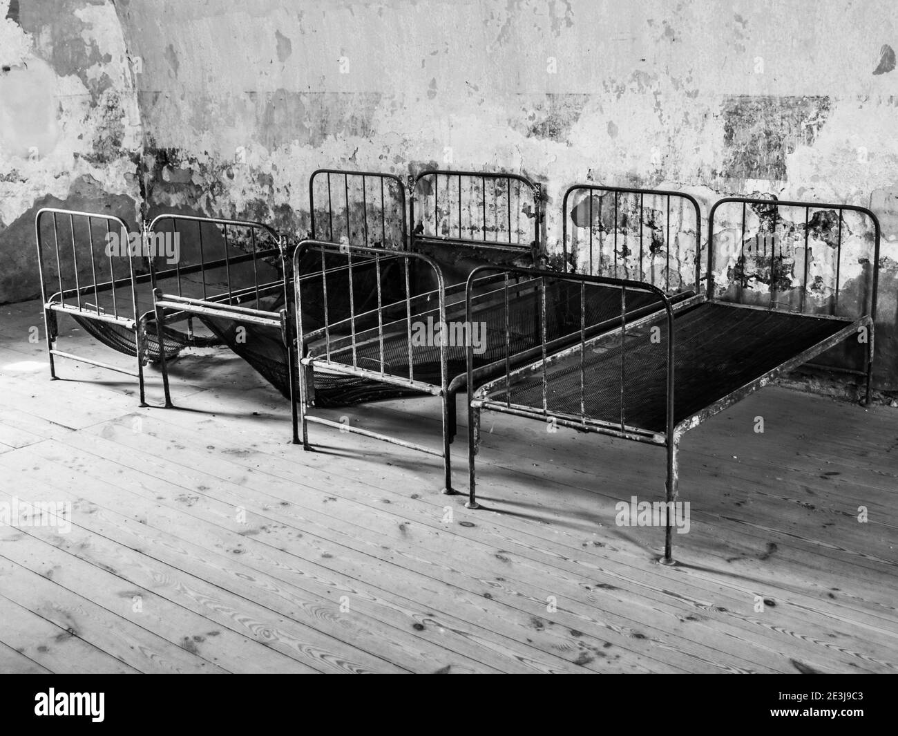 Four old rusty beds in abandoned room. Black and white image Stock Photo