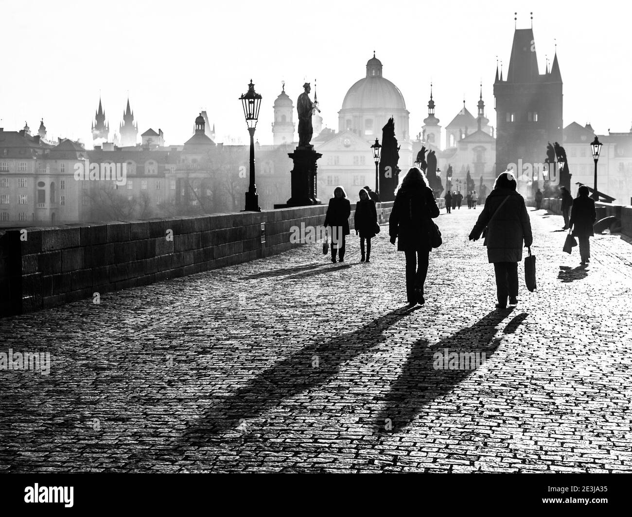 Foggy morning on Charles Bridge, Prague, Czech Republic. Sunrise with silhouettes of walking people, statues and Old Town towers. Romantic travel destionation. Black and white image. Stock Photo