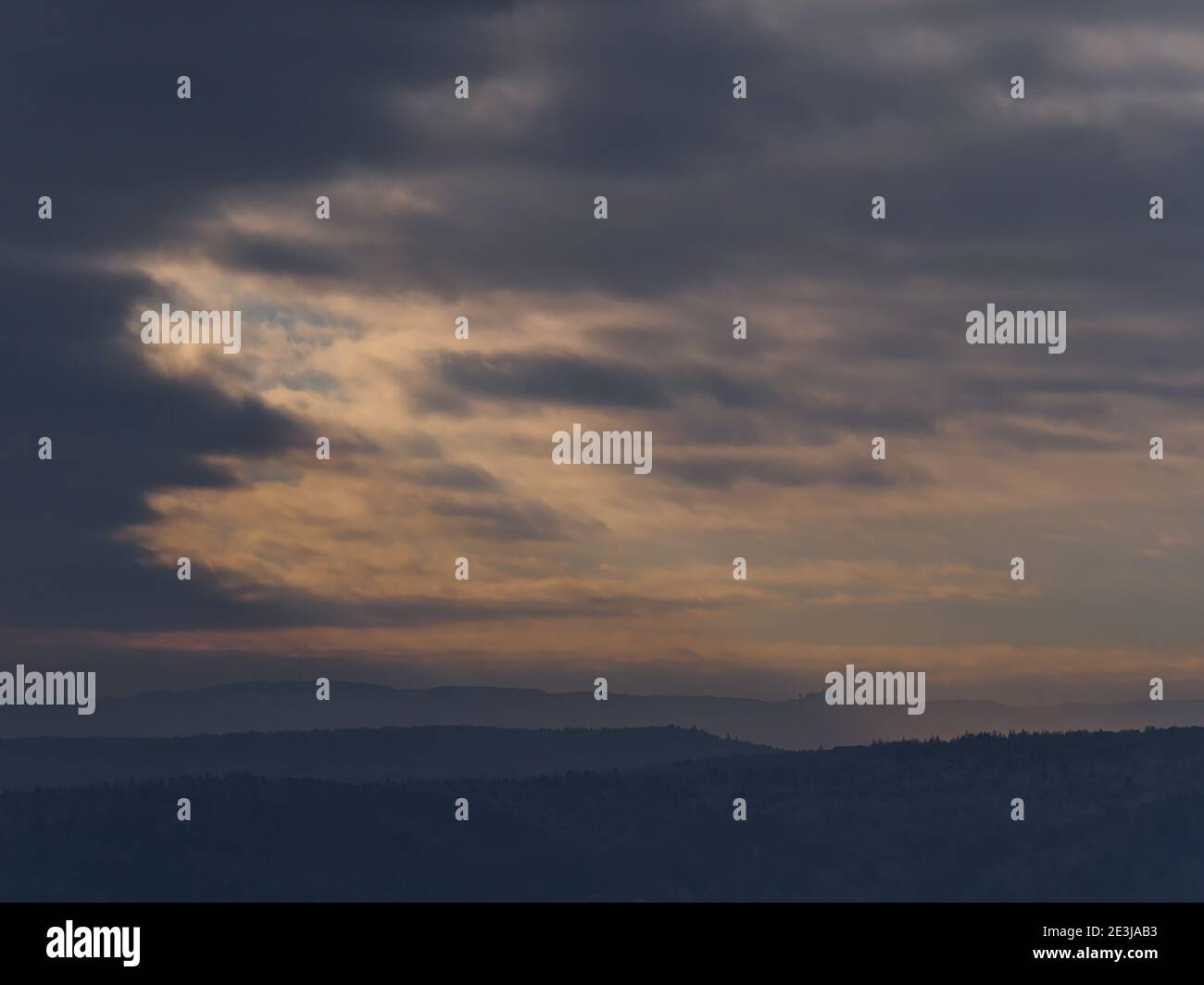 Silhouette of popular historic Hohenzollern Castle on the foothills of low mountain range Swabian Alb below dramatic brightening sky of orange clouds. Stock Photo