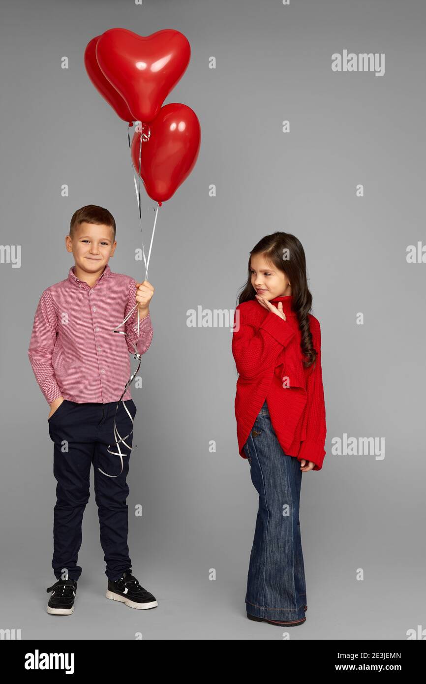 couple of little girl and boy with red heart balloons isolated on gray  background. boy gives shy girl balloon. St. Valentine's Day Stock Photo -  Alamy