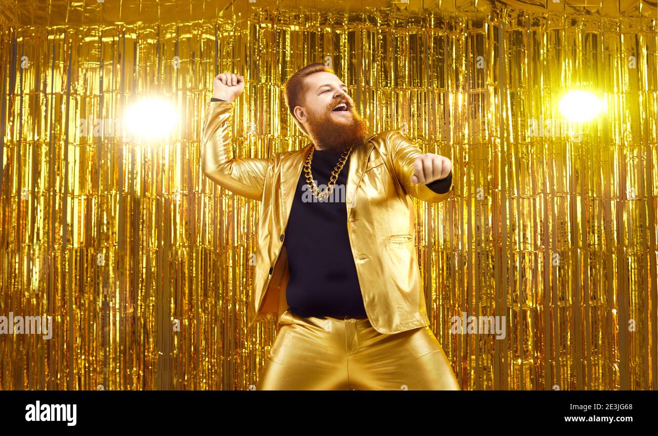 Happy young guy in funny shiny golden suit dancing and having fun at disco party Stock Photo