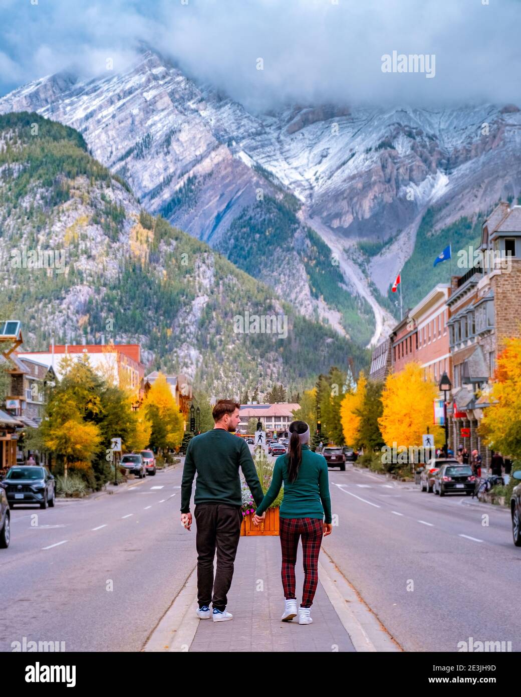 a couple visits the town of Banff Alberta Canada, couple of men, and woman walking at the street of Banff with huge rocky mountains at the background in Canada. Stock Photo
