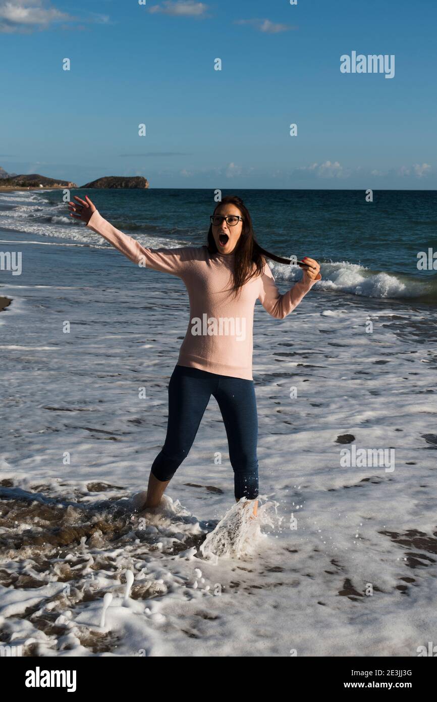 Young woman dressed in casual attire is caught by cold sea wave Stock Photo