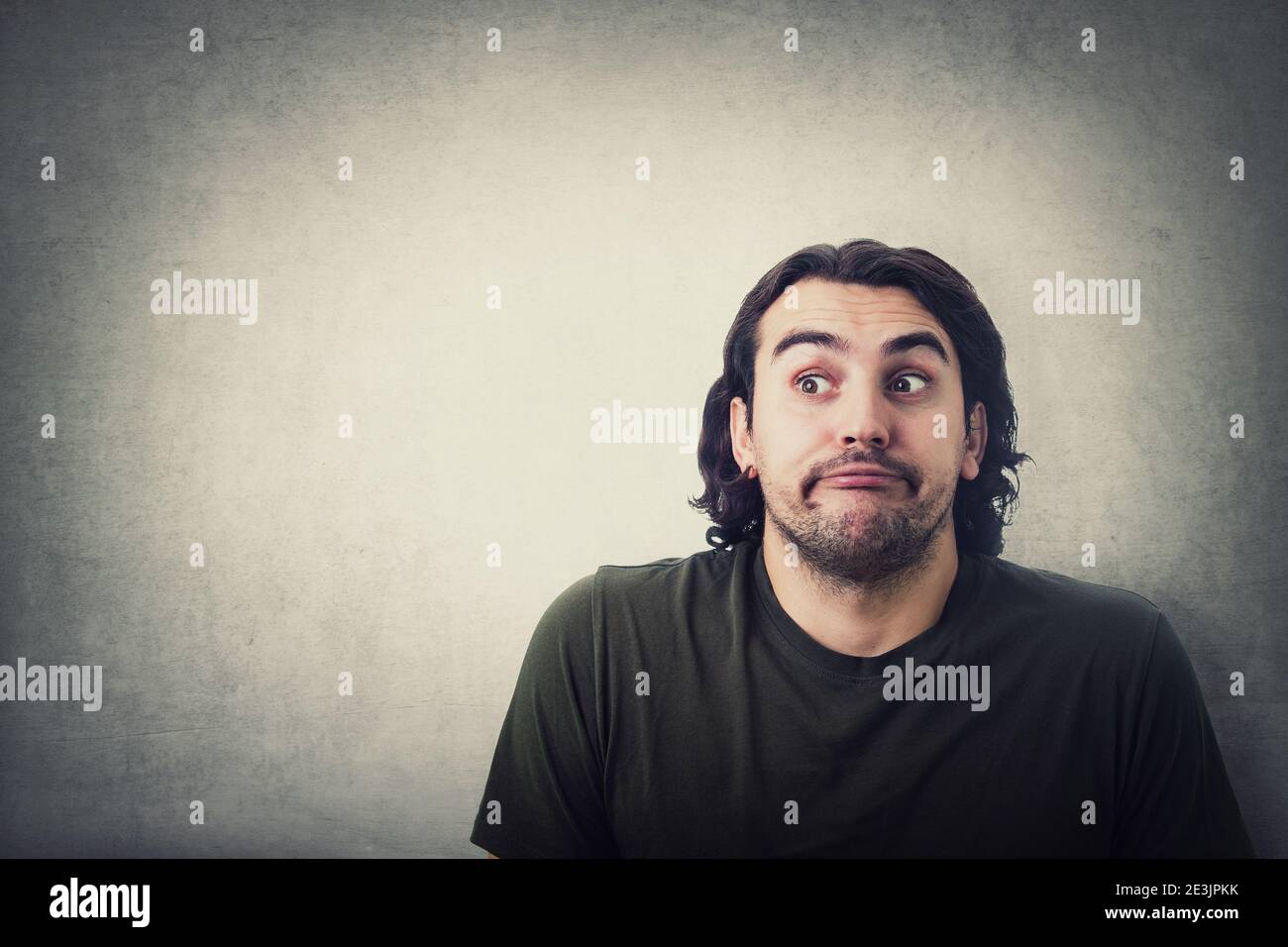 Portrait of naughty young man depicts innocent, funny face expression, looking aside, rolling eyes and hiding his glance isolated on grey wall backgro Stock Photo