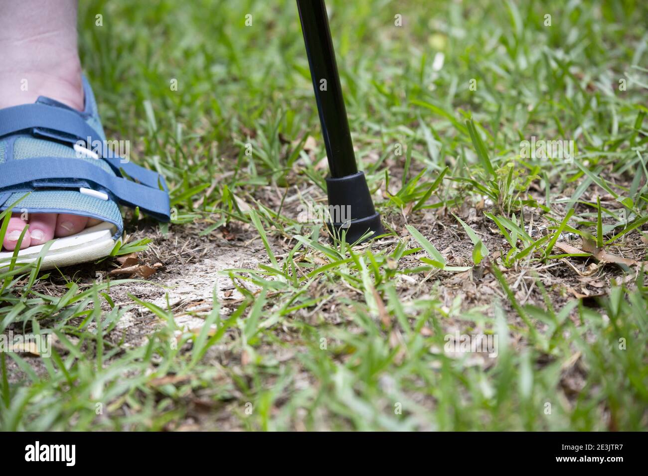 Woman wearing a shoe for a broken foot and walking with a cane Stock